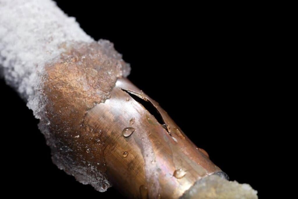 A copper pipe with ice and a large crack, showing water droplets against a black background.
