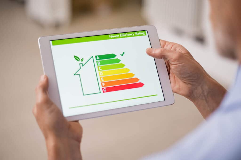 Person holding a tablet displaying a house efficiency rating chart, with categories from A (green) to G (red).