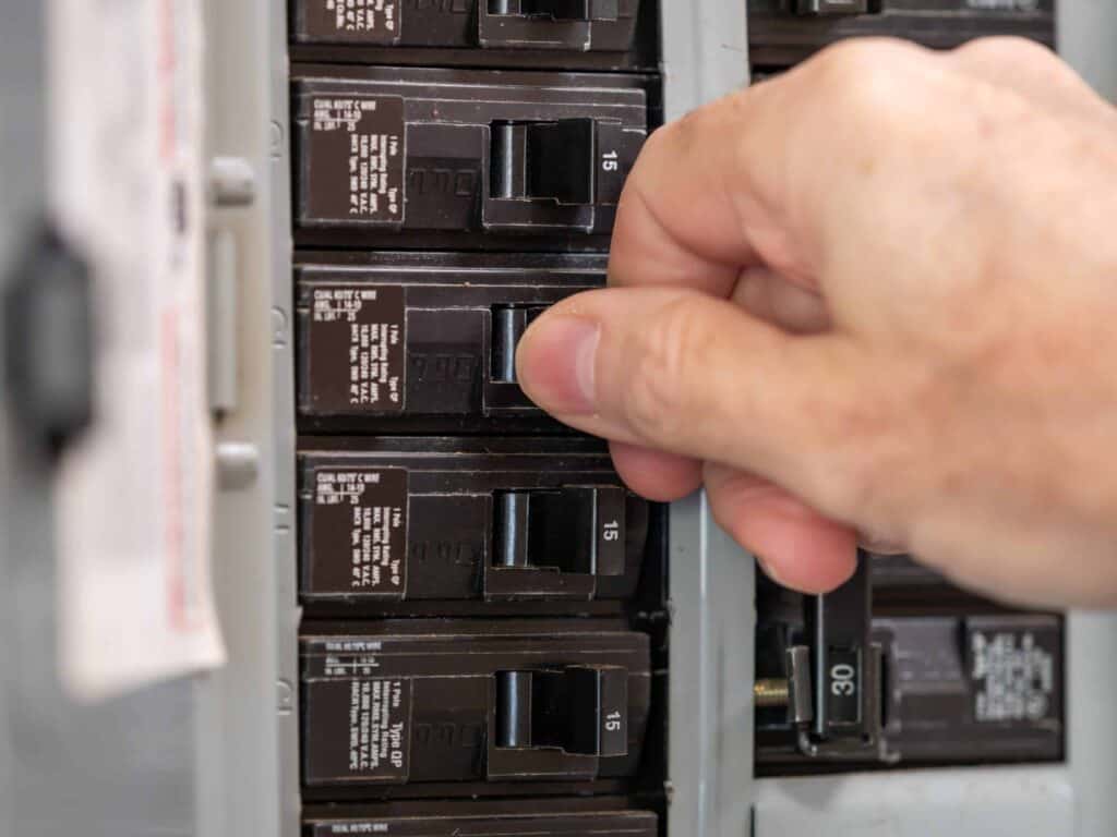 A hand flipping a switch on a circuit breaker panel. Multiple breakers are visible.