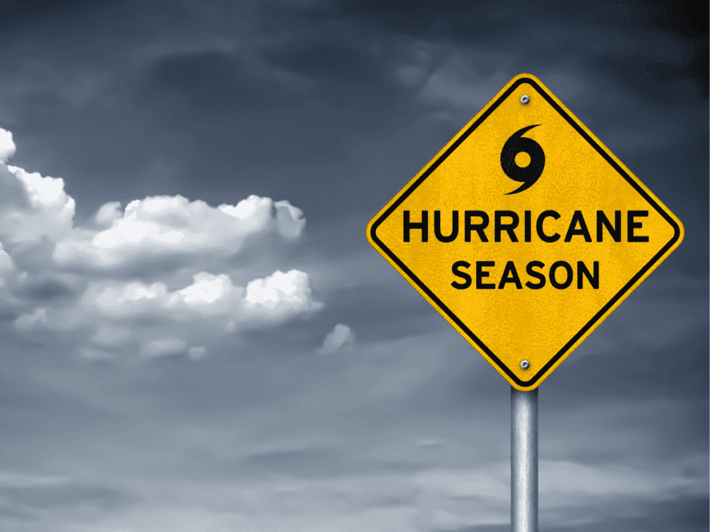 Yellow "Hurricane Season" warning sign with a cyclone symbol against a cloudy sky background.
