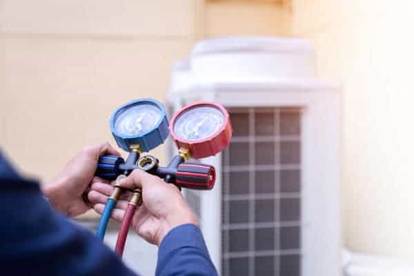 Person adjusting gauges on an HVAC unit outdoors.