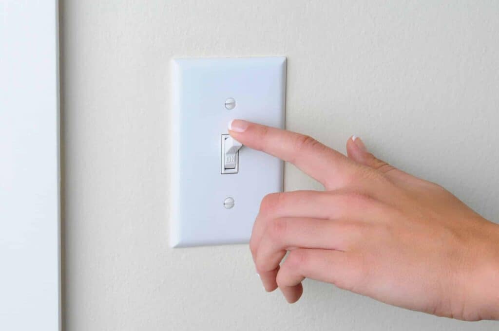 A hand is turning off a white light switch on a wall.