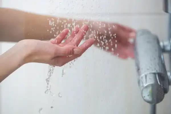 A hand tests the temperature of running water under a showerhead.