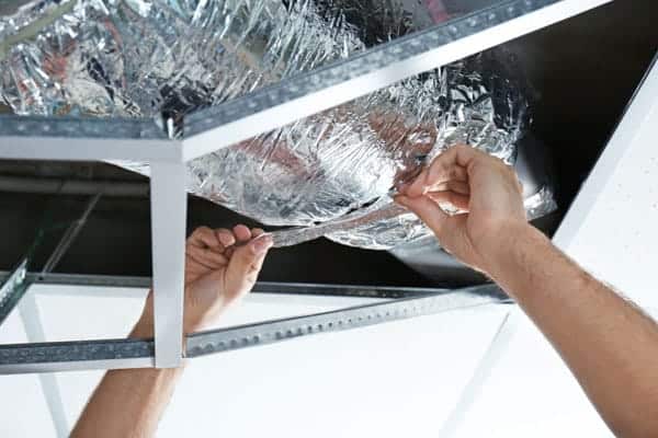 Hands adjusting aluminum ductwork on a ceiling frame.