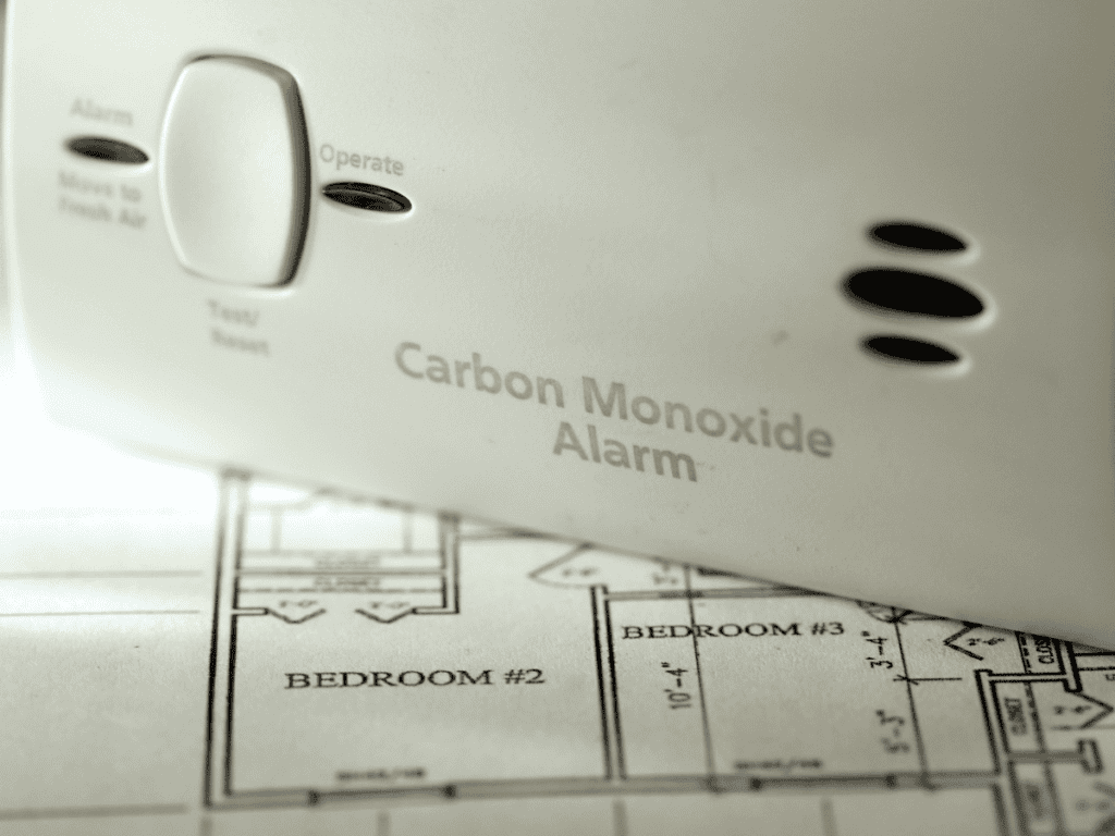Close-up of a carbon monoxide alarm placed on architectural floor plans, highlighting bedrooms. This essential device emphasizes the importance of preventing CO hazards in your home.
