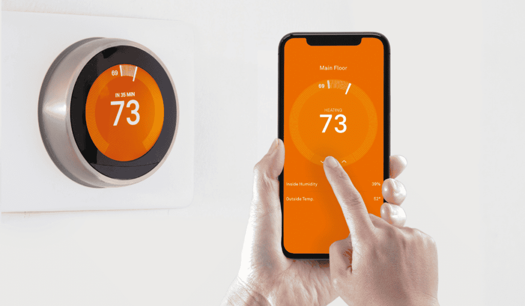 A person sets up a new smart thermostat using a smartphone app. Both screens display "73" degrees in orange, indicating the temperature setting.