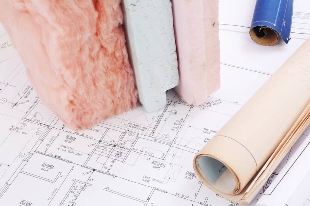 Architectural blueprints with insulation samples and rolled-up plans on top, showcasing the advantages of proper insulation in home design.