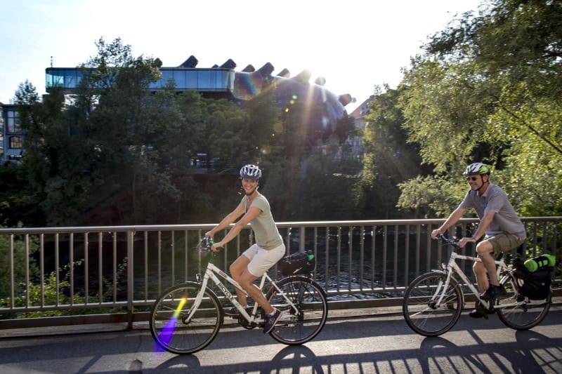 A woman and a man bicycling near a river