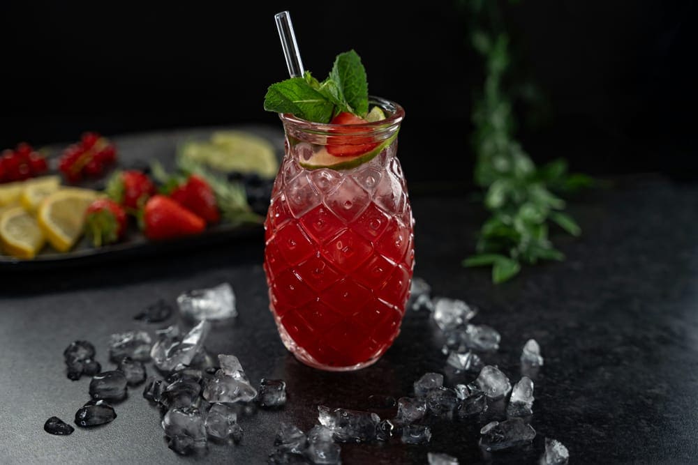 A fruit cocktail surrounded by ice cubes and fresh fruit