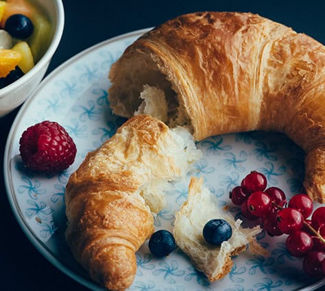 A croissant on a plate with red currants and blueberries