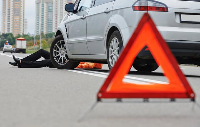 Pedestrian on ground in front of car. Warning red triangles blocking off accident scene.