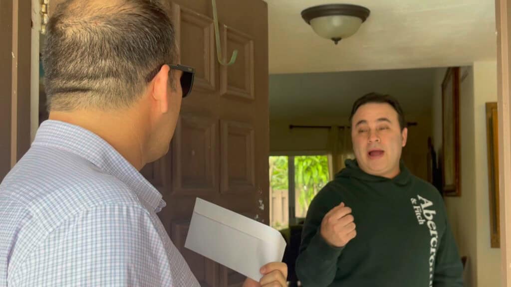 Attorney Justin Ziegler handing a settlement check to a happy client at his home
