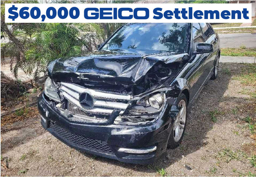 $60,000 GEICO Settlement – A black Mercedes-Benz with severe front-end damage, hood crumpled, and bumper partially detached, parked.