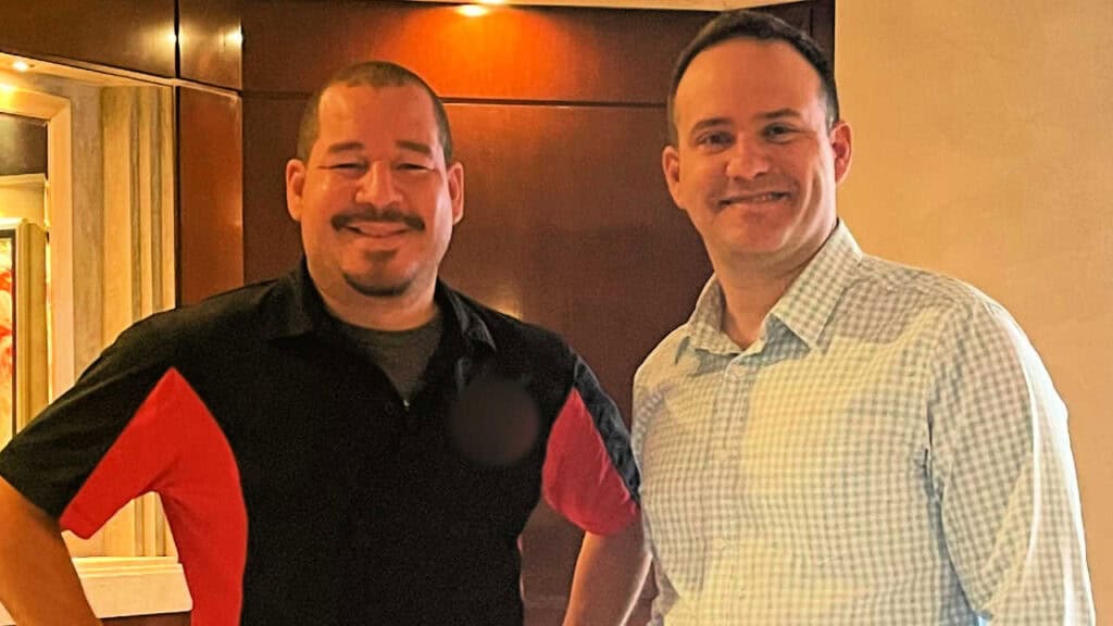 Attorney standing with smiling client just after delivering his GEICO underinsured motorist injury settlement check, both looking happy and relaxed.