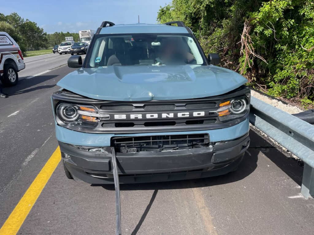 Damaged blue Ford Bronco after a car accident on the highway.