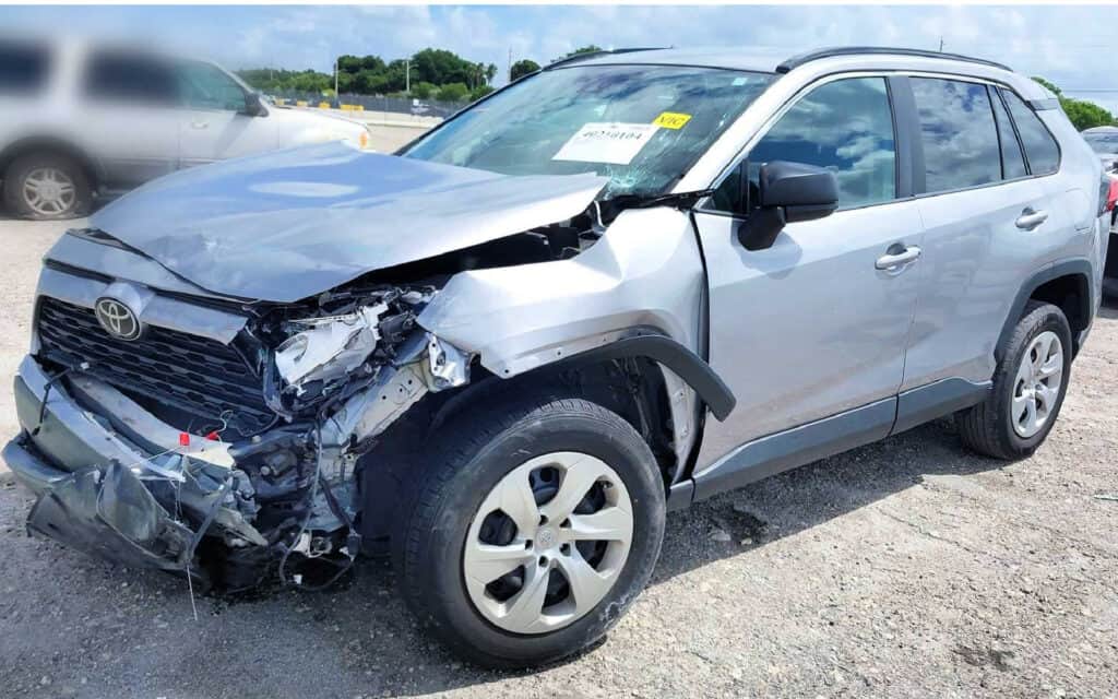 Front view of a severely damaged silver Toyota SUV, showing crumpled hood, bent frame, and significant front-end impact.