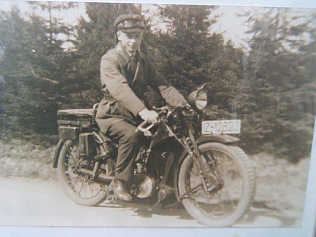 Schwarz-Weiß-Bild eines Mannes auf einem alten Motorrad unterwegs.