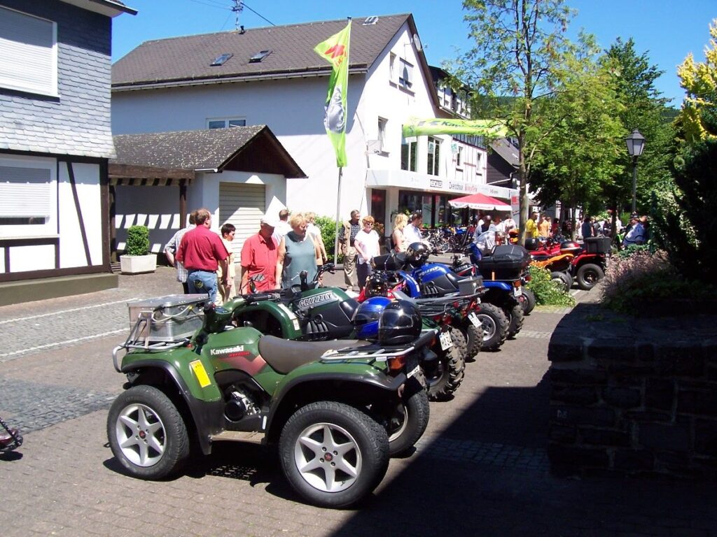 Motorräder und Quads parken in einer Stadtstraße, Menschen spazieren vorbei.