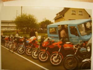 Mehrere Motorräder und ein Bus vor einem Wohnhaus bei einem Treffen.