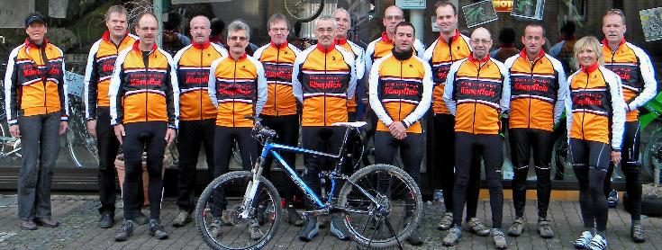 Gruppe von Radfahrern in orange-weißen Trikots mit Fahrrad im Vordergrund.