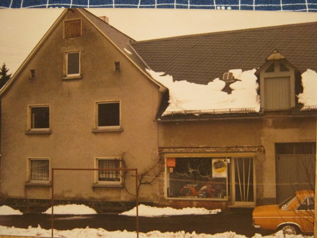 Altes Haus im Winter mit Schneedecke und einem alten Auto davor.