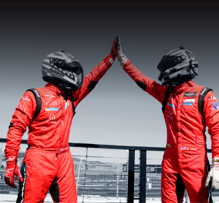 Two race car drivers in red suits high-fiving at the track.