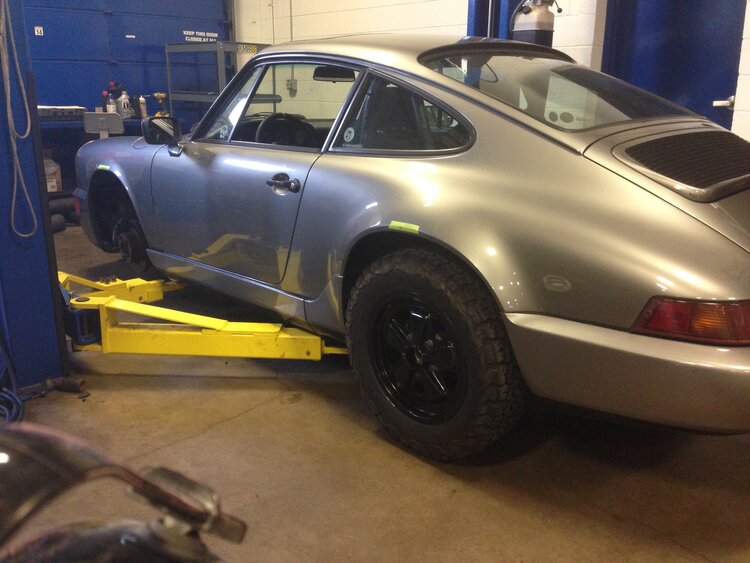Silver 1990 Porsche 964 C4 parked indoors with black wheels and classic design.