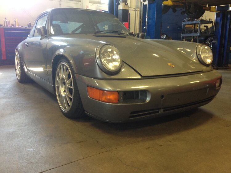 Gray 1990 Porsche 964 C4 parked in a garage with blue equipment in the background.