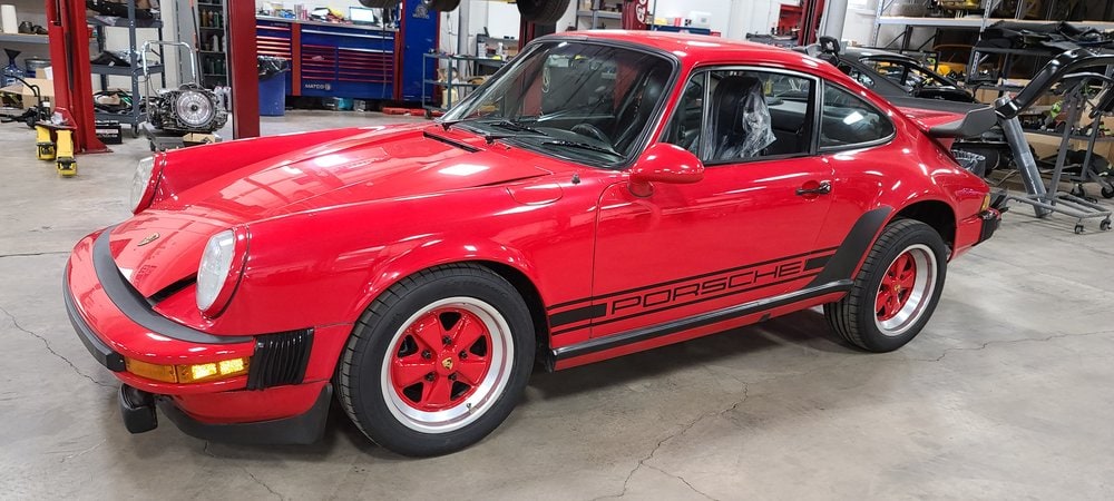 Red 1975 Porsche 911 with black stripe in workshop setting.