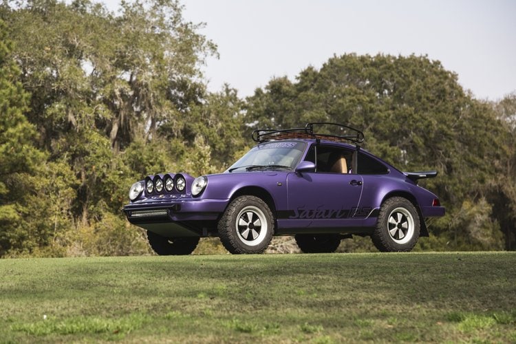 Purple 1991 Porsche 964 C4 with off-road accessories on grassy field.