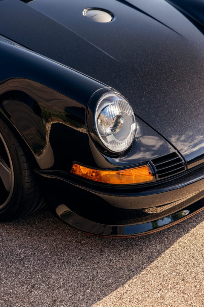 Close-up of black 1989 Porsche 964 headlight and front bumper.