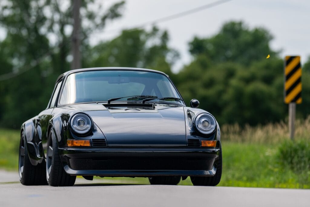 1989 Porsche 964 sports car parked outdoors with greenery in background.