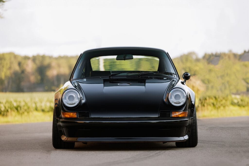 Black 1989 Porsche 964 sports car on open road with scenic background.