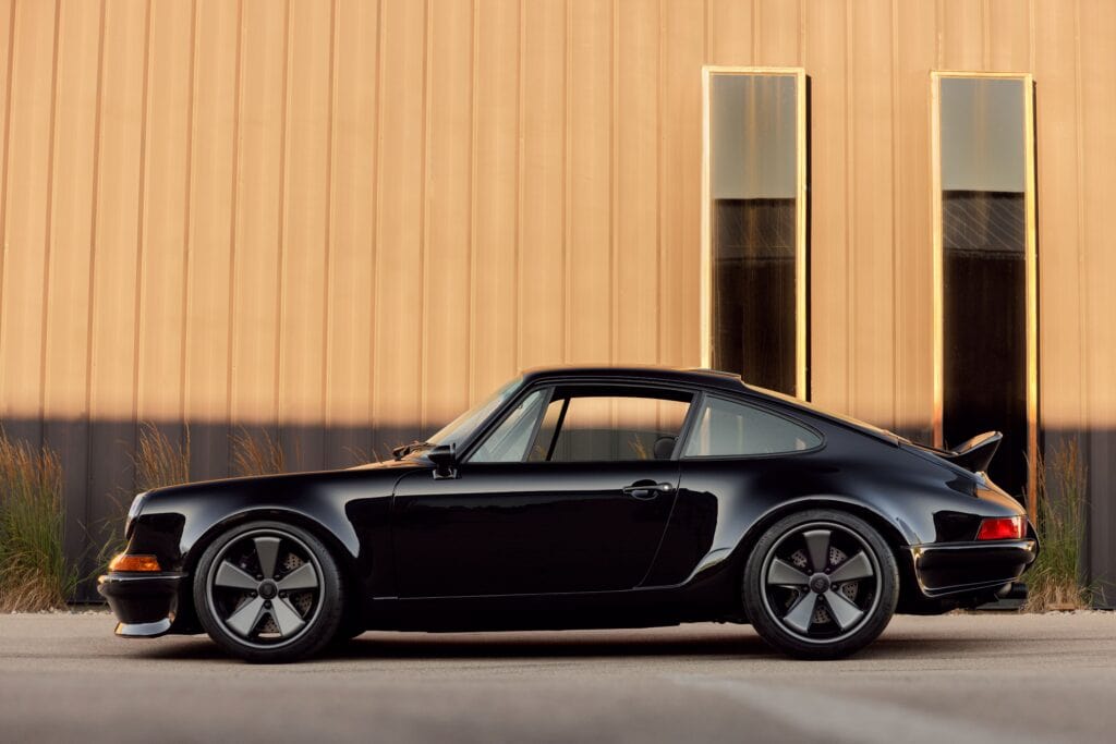 Black 1989 Porsche 964 sports car parked outside modern building.