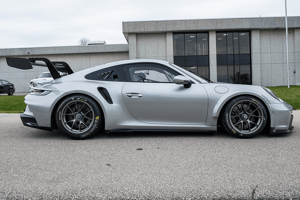 Silver Porsche 911 GT3 Cup 992 parked outside modern building.