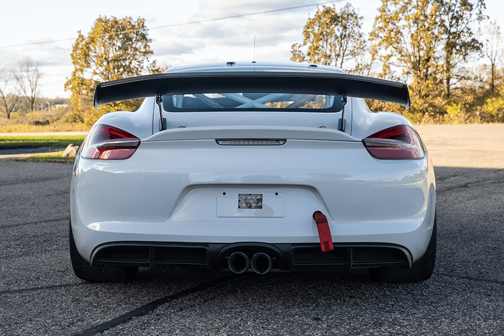 Rear view of a white Porsche 981 Clubsport MR with a large rear wing and dual exhausts.