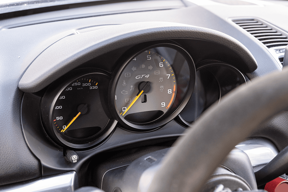 Close-up of Porsche 981 GT4 dashboard with speedometer and tachometer.