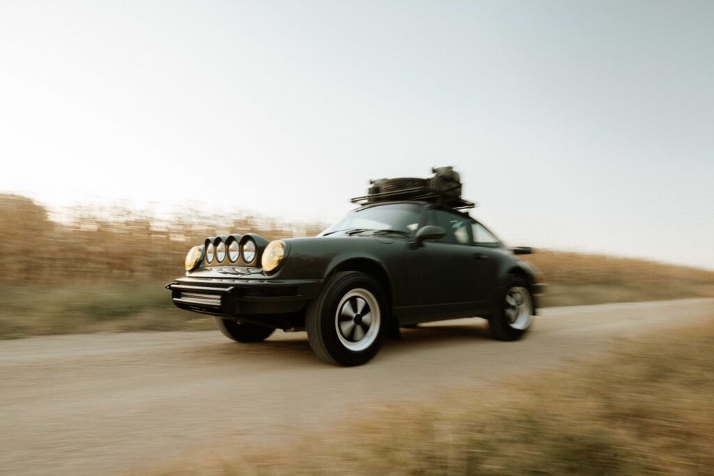 Kellymoss Porsche 964 driving on a rural road with luggage on roof.