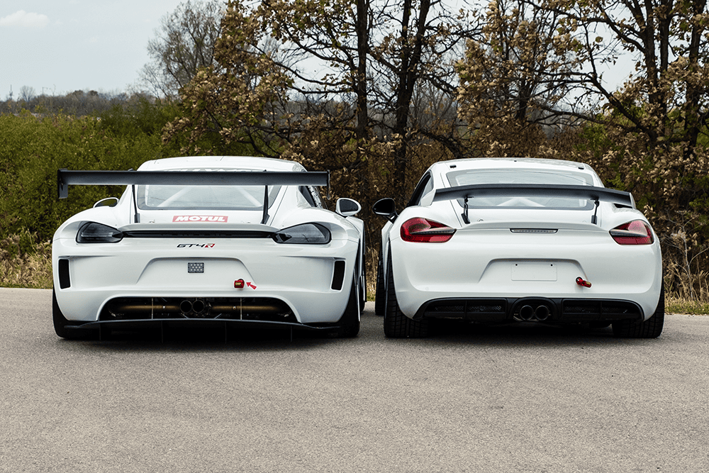 Two white Kellymoss GT4R race cars parked on a road with trees in the background.