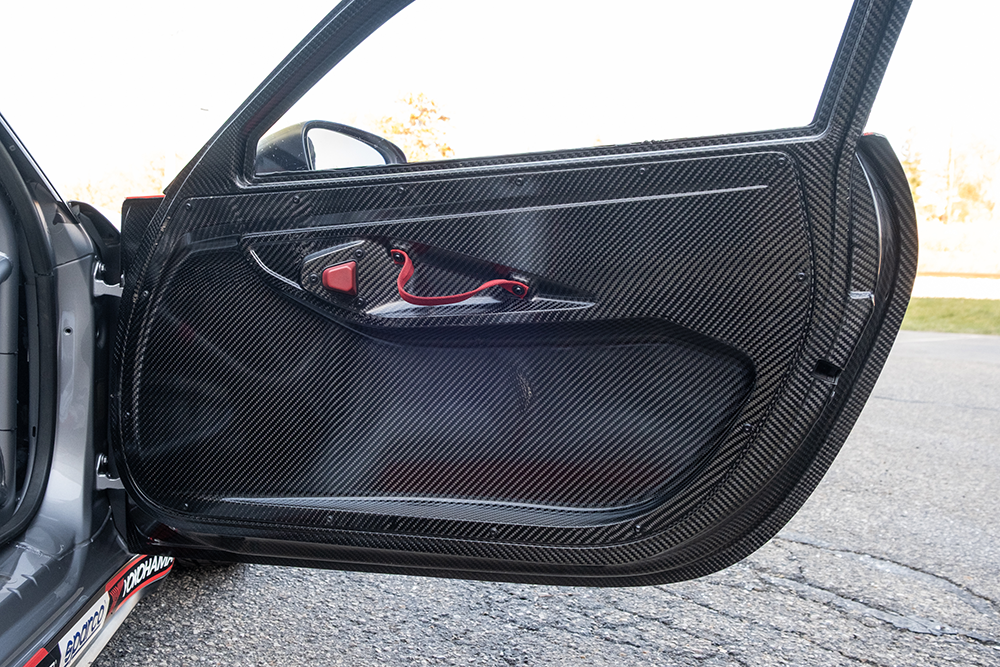 Close-up of a carbon fiber car door panel with red safety latch.