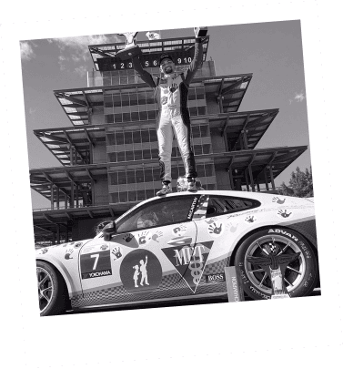 Race car driver celebrating victory on top of a sports car.