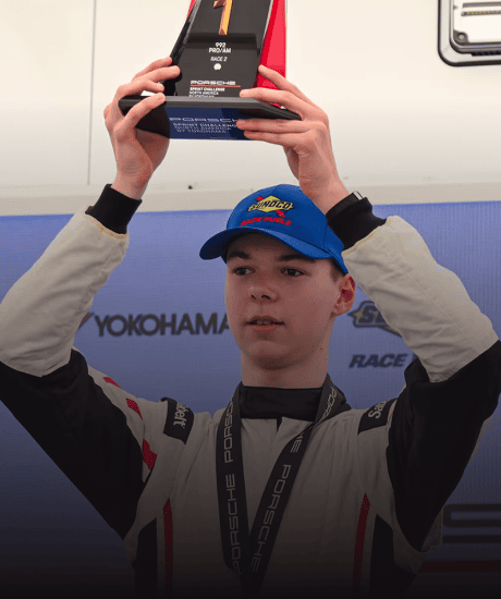 Young race car driver holding a trophy at Porsche Sprint Challenge event.