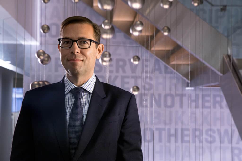 Businessman in a modern office setting with glass walls and stylish lighting fixtures.