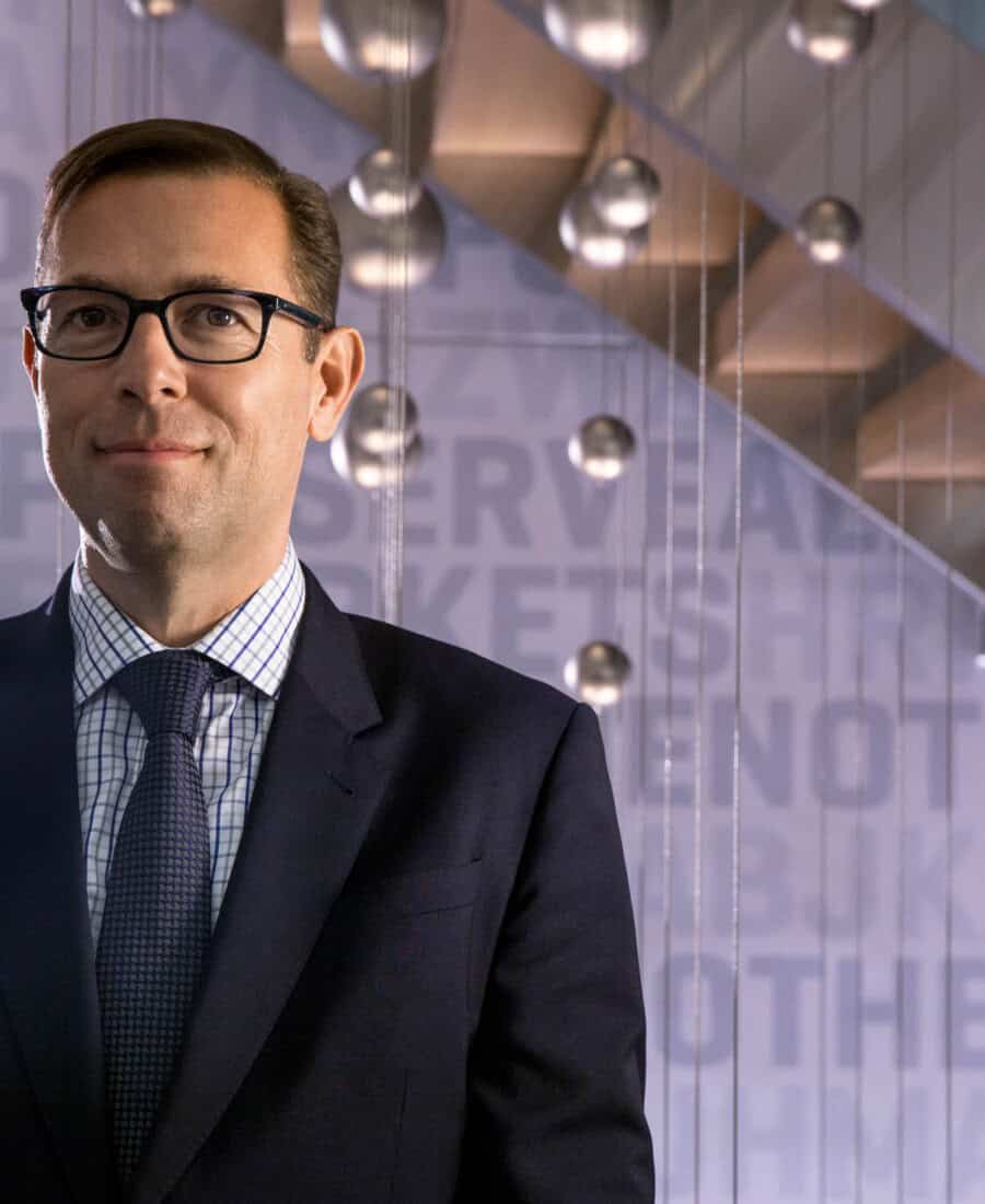 Businessman in a modern office setting with glass walls and stylish lighting fixtures.