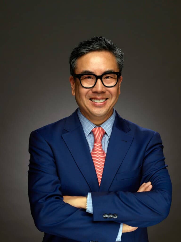 Confident professional man in formal suit with glasses smiling, arms crossed.