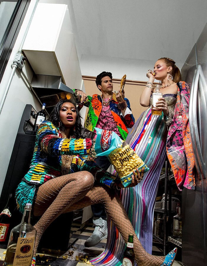 Fashion models in colorful outfits in a small room with snacks and drinks.