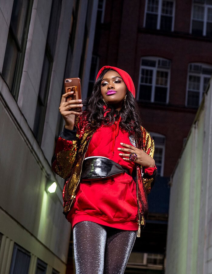 Fashionably dressed woman taking a selfie in an urban alleyway.