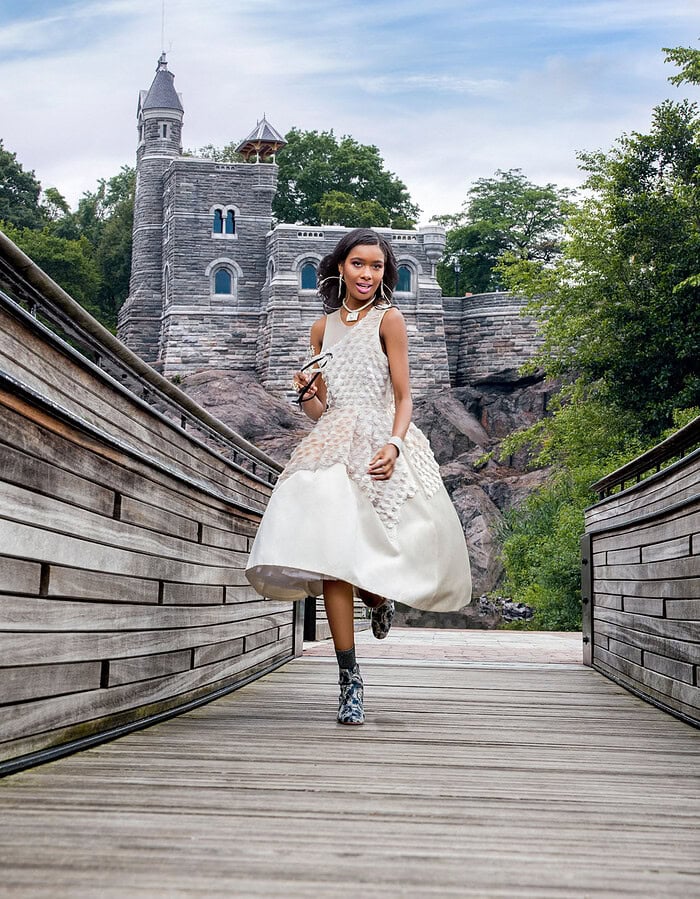 Young girl in elegant dress walking on a wooden bridge near a castle.