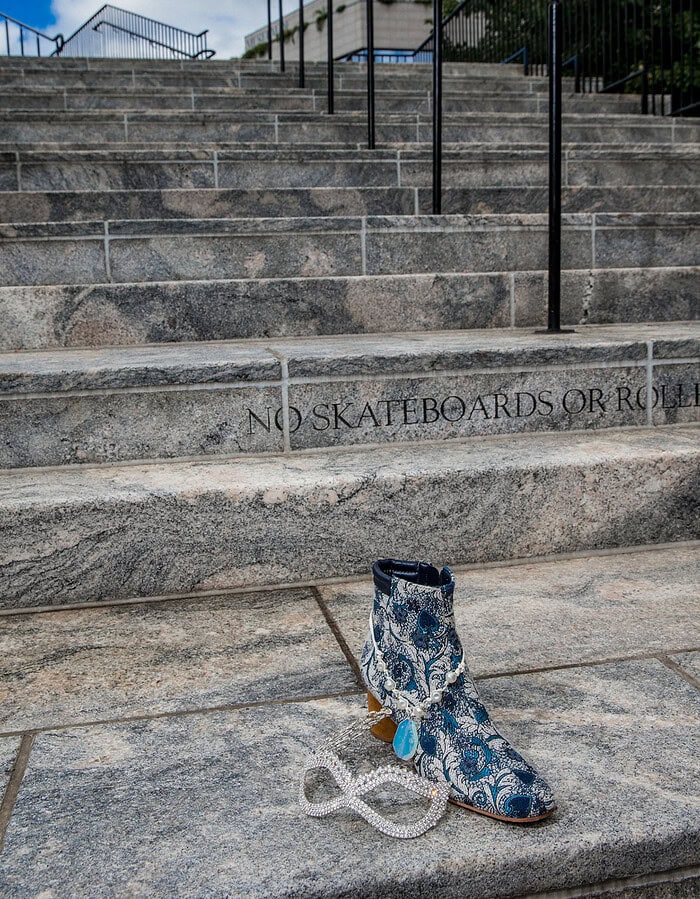 Decorative blue and white patterned boot on stone steps with railing and trees.