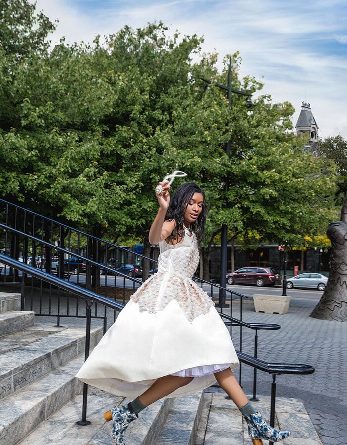 Fashion-forward woman in a white dress and patterned boots on city stairs.